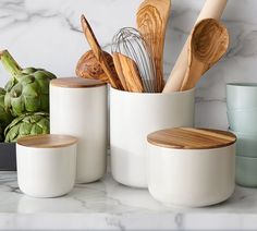 kitchen utensils and wooden spoons in white ceramic containers on marble countertop