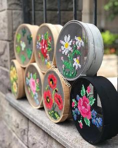 several wooden barrels with cross stitch flowers on them are sitting next to a wrought iron fence