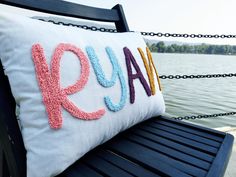 a pillow with the word ryan on it sitting on a bench next to some water