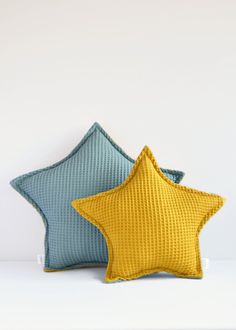 two yellow and blue stars are sitting side by side on a white surface, one is made out of knitted fabric