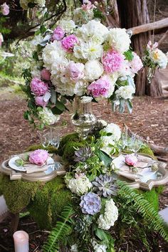 a table topped with lots of flowers and greenery next to a forest filled with trees