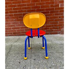 a yellow and blue plastic chair sitting on top of a sidewalk next to a brick wall