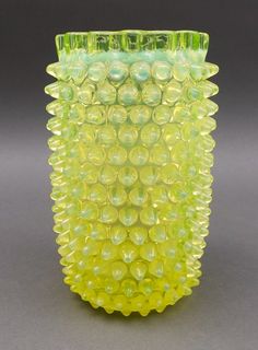 a yellow glass vase sitting on top of a table next to a gray wall and floor