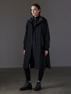 Front angled full-body view of woman wearing Kite Packable Rain Poncho in Onyx Black from AETHER Apparel.