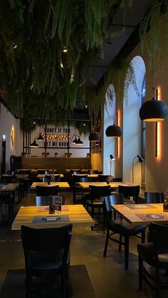 the interior of a restaurant with tables, chairs and plants hanging from the ceiling above