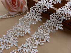 white lace with flowers and pearls on a table next to a pink rose in a wooden box