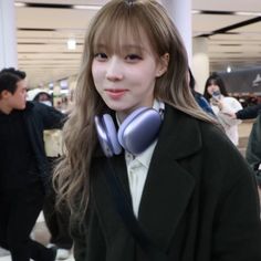 a young woman with ear phones on her neck in an airport terminal, looking at the camera