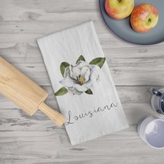 a kitchen towel with an image of a flower on it next to two apples and a teapot