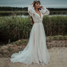 a woman in a wedding dress standing on a dirt road with her arms behind her head