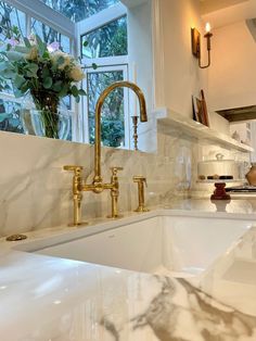 a white kitchen with marble counter tops and gold faucets on the sink area