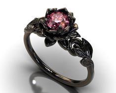 "If you're looking for an engagement ring like no other, stop right here. This AMAZING piece of fine jewelry is the perfect expression of your eternal love. Its BLACK colors bring out the beauty of this ring. This engagement ring is created of gleaming, 14kt black gold, carved into an elaborate leaf design at the top. A striking Pink Sapphire sits boldly at the center, surrounded by black gold petals, forming the eye-catching image of a lotus flower. Item Specifics: (1 Ring Only) Gem Details: Ce Pink And Black Engagement Ring, Black And Pink Wedding Rings, Elegant Black Flower Promise Ring, Elegant Black Flower Ring For Anniversary, Elegant Black Flower Ring, Black Sapphire Ring With Brilliant Cut As Gift, Black Sapphire Ring With Brilliant Cut For Gift, Gift Black Sapphire Ring With Brilliant Cut, Black Flower Ring For Wedding