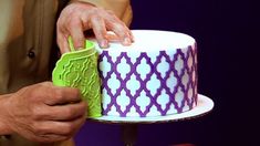 a man is decorating a cake with purple and green icing on the top