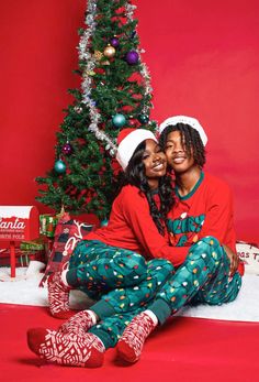 two people sitting next to each other in front of a christmas tree