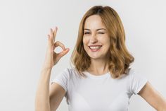 a woman is making the peace sign with her hands and smiling at the camera while standing against a white background