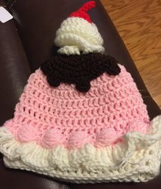 a crocheted pink and white hat with a black bow on top sitting on a brown leather chair