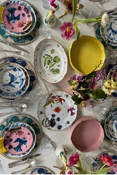 a table topped with lots of different colored plates and bowls filled with flowers on top of it