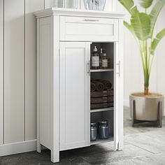 a white cabinet with towels and other items in it next to a potted plant