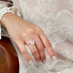 a woman's hand with a pink diamond ring on her finger, wearing a white lace dress