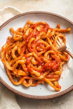 a white plate topped with pasta covered in marinara sauce and a wooden spatula