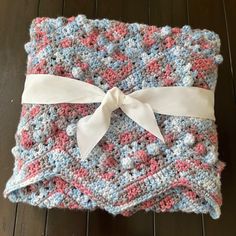 a crocheted blanket with a white bow on the top and pink, blue, and gray colors