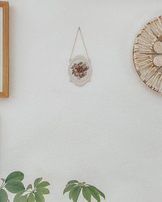 two clocks on the wall next to a plant and other items hanging from it's sides