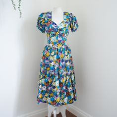 A gorgeous multi-coloured floral 1980s vintage dress. It has a gorgeous neckline and slightly puffy sleeves. There are shoulder pads which could be taken out. It fastens with buttons down the front and the skirt gathers at the waist. So cute! And it has pockets! Viscose and cotton mix. No flaws to note.  Bust: 34" Waist: 30" Length: 45" ♥ SHIPPING ♥ * International postage - these costs are estimates, and I will happily refund any excess postage you may have paid once I have posted the item. * * UK postage - all items will be sent via Royal Mail* ♥ DESCRIPTIONS ♥ I thoroughly inspect all of my items and aim to describe them as accurately as possible, making any noticeable flaws known. But please remember that items are between 30 and 85 years old, so may have tiny flaws that aren't noticea Multicolor Fitted Puff Sleeve Dress With Floral Print, Fitted Multicolor Puff Sleeve Dress With Floral Print, Fitted Multicolor Floral Print Puff Sleeve Dress, Multicolor Puff Sleeve Dress For Garden Party, Summer Floral Print Vintage Dress With Puff Sleeves, Summer Vintage Dress With Floral Print And Puff Sleeves, Summer Floral Vintage Dress With Puff Sleeves, Vintage Multicolor Puff Sleeve Dress, Retro Multicolor Floral Print Midi Dress