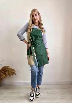 a woman standing in front of a white wall wearing an apron and black converses