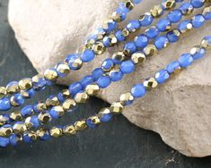 two strands of blue and gold beaded necklaces sitting on top of a rock