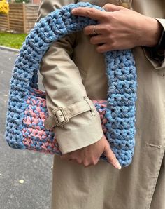 a person holding a crocheted blue and pink handbag on the side of a road