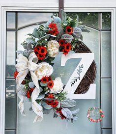 a wreath is hanging on the front door of a house with red and white flowers