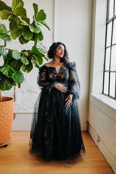 a woman standing in front of a window wearing a black dress and holding her hands on her hips