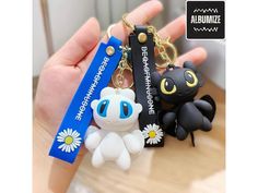 a person holding two different key chains in front of their hand, one with an animal and the other has a flower on it