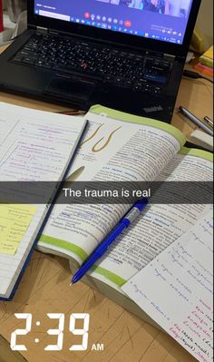 a laptop computer sitting on top of a desk next to an open book and pen