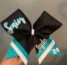 a person holding up a black and blue cheer bow with the word senior on it