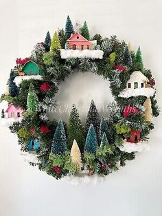 a christmas wreath hanging on the wall with houses, trees and snowflakes around it