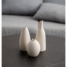 three white vases sitting on top of a table in front of a gray couch