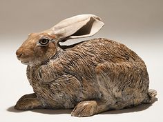 a statue of a brown rabbit sitting on top of a white table next to a gray wall