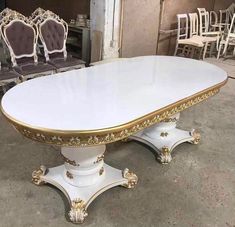 a large white table with gold trimmings and chairs in front of it on the ground