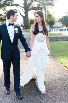 a man and woman holding hands walking down a sidewalk