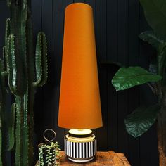 an orange lamp sitting on top of a wooden table next to a potted plant