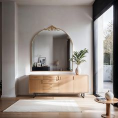 a large mirror sitting on top of a wooden cabinet in a living room next to a window