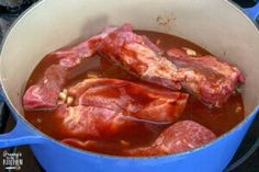 some meat is cooking in a blue pot on the stove top with water and spices