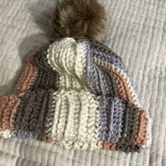 a crocheted hat with a pom - pom sits on a bed