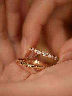 a close up of a person's hand holding two gold rings with diamonds on them