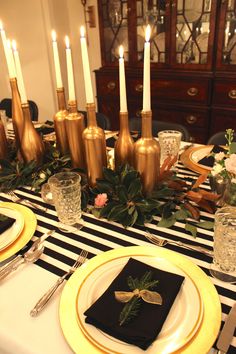 the table is set with black and white striped cloths, gold place settings, candles, and greenery