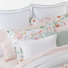 a white bed with pink and green flowers on it's comforter, along with matching pillows