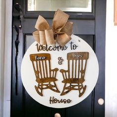 a welcome sign with two rocking chairs on it and a bow hanging from the front door