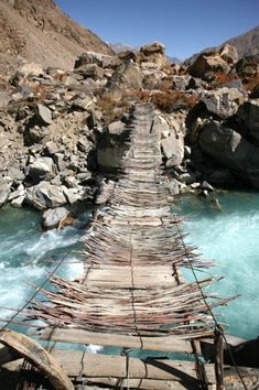 a long wooden bridge over a river with rocks and water in the backround