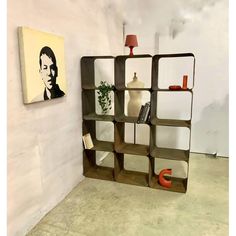 a shelf with books and vases on it next to a wall mounted portrait in the corner