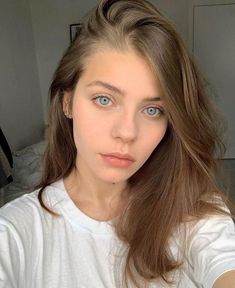 a woman with blue eyes is taking a selfie in front of the camera while wearing a white t - shirt